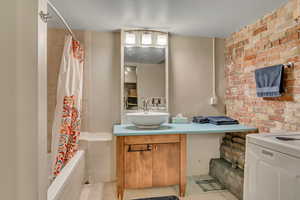 Full bathroom with vanity, tiled shower / bath, tile patterned flooring, and brick wall