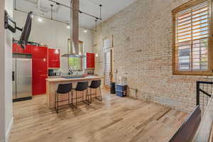 Kitchen with stainless steel fridge with ice dispenser, a high ceiling, brick wall, light wood-style flooring, and track lighting