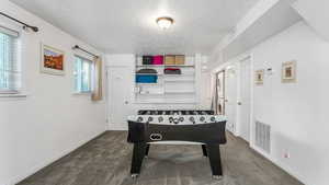 Playroom with a textured ceiling, dark colored carpet, and baseboards