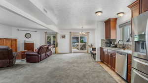 Kitchen featuring stainless steel appliances, a sink, a chandelier, open floor plan, and light carpet