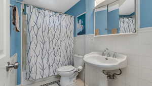 Bathroom with toilet, a sink, tile walls, tile patterned floors, and shower / bath combo