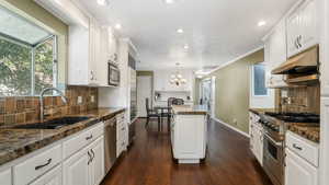 Kitchen featuring stainless steel appliances, a sink, a center island, a chandelier, and white cabinetry