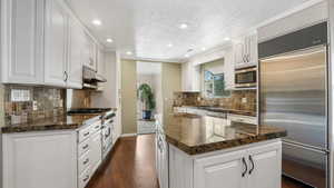 Kitchen with premium appliances, a kitchen island, a sink, dark wood-style floors, and recessed lighting