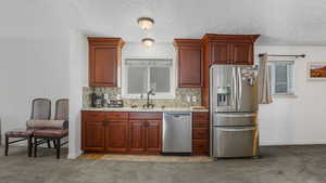 Kitchen with stainless steel appliances, a sink, light colored carpet, decorative backsplash, and a textured ceiling