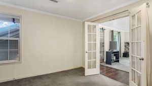 Empty room with french doors, carpet flooring, crown molding, baseboards, and wood finished floors