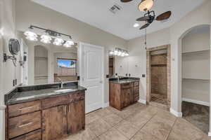 Full bathroom with a ceiling fan, tiled shower, two vanities, baseboards, and a walk in closet