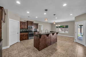 Kitchen featuring appliances with stainless steel finishes, a kitchen breakfast bar, baseboards, dark brown cabinets, and recessed lighting