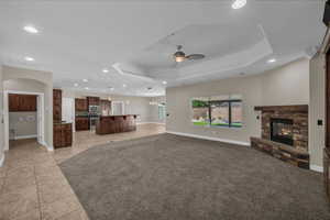 Unfurnished living room with a fireplace, ceiling fan, recessed lighting, a tray ceiling, and baseboards