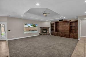 Unfurnished living room featuring a ceiling fan, tile patterned flooring, recessed lighting, a raised ceiling, and baseboards
