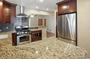 Kitchen with appliances with stainless steel finishes, wall chimney range hood, a peninsula, a ceiling fan, and backsplash
