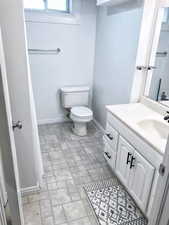 Full bath with baseboards, brick patterned floors, vanity, and toilet