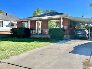 View of front of home featuring a porch, concrete driveway, a front lawn, an attached carport, and brick siding