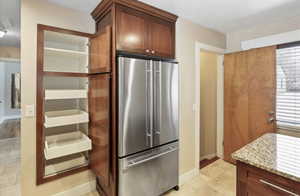 Kitchen featuring stainless steel refrigerator, light stone counters, baseboards, and healthy amount of natural light