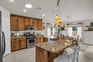 Kitchen featuring appliances with stainless steel finishes, a sink, brown cabinetry, a kitchen breakfast bar, and light tile patterned flooring