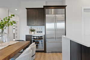 Kitchen with stainless steel Subzero fridge, built-in beverage cooler, dark wood cabinetry, light quartz countertops, and LVP flooring.