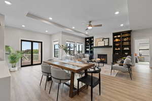 Open concept dining space and living room featuring LVP flooring, tray ceiling, recessed lighting, gas fireplace, and built-in bookshelves.