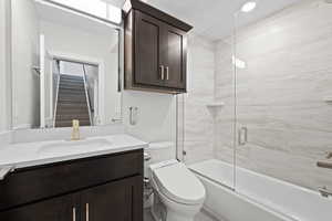 Full bathroom with Toto toilet, dark wood vanity, and combined bath / shower with frameless glass door