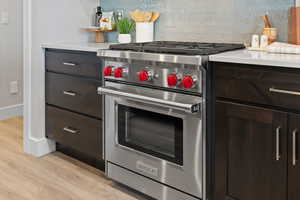 Designer Wolf range, light quartz countertops, tile backsplash, and dark wood cabinetry.