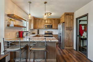 Kitchen with appliances with stainless steel finishes, dark wood finished floors, a sink, a peninsula, and light stone countertops