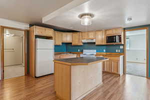 Kitchen featuring white appliances, under cabinet range hood, light wood-style flooring, and light brown cabinets