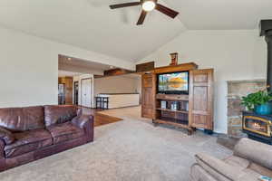 Carpeted living room with a wood stove, a ceiling fan, and vaulted ceiling