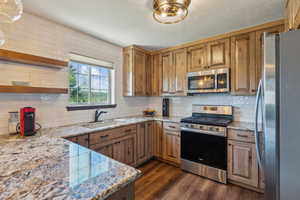 Kitchen featuring appliances with stainless steel finishes, a sink, open shelves, and decorative backsplash