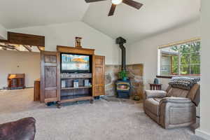 Carpeted living area with lofted ceiling, ceiling fan, and a wood stove