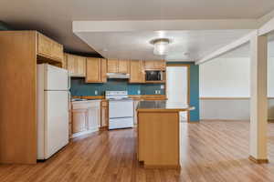 Kitchen featuring white appliances, under cabinet range hood, light wood finished floors, a sink, and light brown cabinetry
