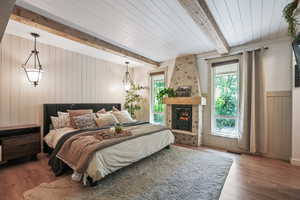 Bedroom featuring beam ceiling, wood finished floors, a stone fireplace, and wood walls