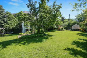View of grassy yard with a playground and a mountain view
