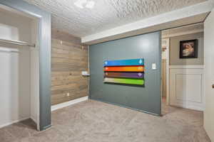 Unfurnished bedroom with carpet floors, wooden walls, a textured ceiling, and baseboards