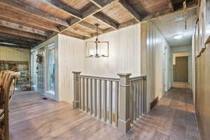 Hall featuring wood finished floors, wood ceiling with exposed beams, an upstairs landing, wood walls, and a chandelier