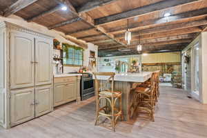 Kitchen featuring stainless steel range, wood ceiling with exposed beams, light wood-style floors, light countertops, and open shelves