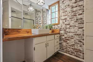 Bathroom with wood finished floors, vanity, baseboards, a stall shower, and brick wall
