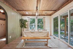 Dining room featuring wooden ceiling with exposed beams, arched walkways, wood walls, and wood finished floors