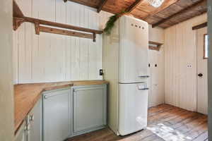 Kitchen with freestanding refrigerator, wood counters, wood ceiling with exposed beams, hardwood / wood-style flooring, and wood walls