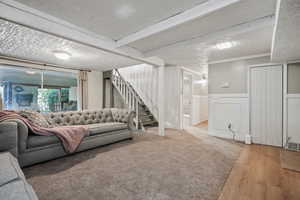 Living area featuring stairs, wainscoting, wood finished floors, a textured ceiling, and a decorative wall