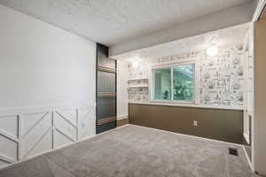 Carpeted spare room featuring a textured ceiling and wainscoting