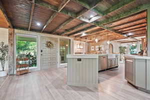 Kitchen featuring light countertops, light wood-style flooring, a large island, and wood ceiling with exposed beams