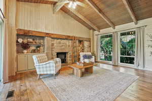 Living area with wooden ceiling with exposed beams, high vaulted ceiling, light wood-style flooring, ceiling fan, and wooden walls
