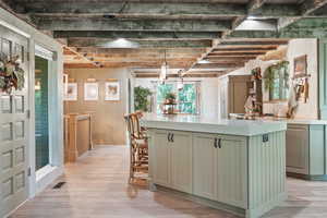 Kitchen with green cabinetry, a center island, light wood finished floors, light countertops, and beamed ceiling