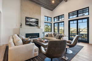 Living room with high vaulted ceiling, a high end fireplace, wooden ceiling, wood finished floors, and baseboards