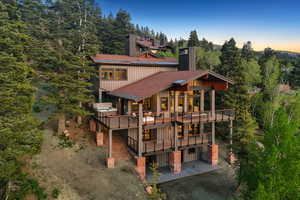 Rear view of house featuring a patio, board and batten siding, a wooden deck, a view of trees, and a balcony