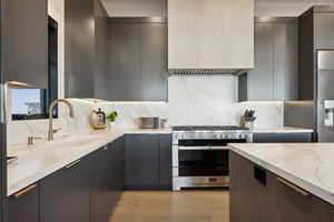 Kitchen with appliances with stainless steel finishes, a sink, light stone counters, modern cabinets, and gray cabinetry