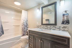 Full bathroom featuring decorative backsplash, vanity, toilet, shower / tub combo with curtain, and tile patterned flooring