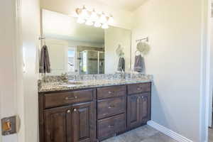 Bathroom with double vanity, a shower stall, tile patterned flooring, and baseboards