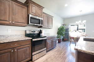Kitchen featuring appliances with stainless steel finishes, a chandelier, light wood-style flooring, a sink, and light stone counters