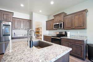 Kitchen with appliances with stainless steel finishes, light wood-style flooring, light stone countertops, a sink, and recessed lighting