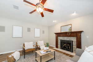 Living room with wood finished floors, a ceiling fan, a stone fireplace, and baseboards