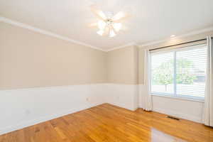 Empty room featuring light wood finished floors, baseboards, wainscoting, ornamental molding, and a ceiling fan